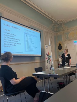 Das Foto zeigt Frau Schulz bei ihrem Vortrag zum Thema Findb&uuml;cher & Information Retrieval. Gerade erkl&auml;rt sie den Begriff Tektonik. Hierf&uuml;r zeigt mit einem Laserpointer auf die Vortragspr&auml;sentation auf einer Leinwand.