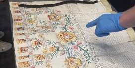 Das Foto zeigt einen kunstvoll gestalteten historischen Stammbaum einer Adelsfamilie, der der Einf&uuml;hrung in die Adelsarchivpflege diente. Eine behandschuhte Hand deutet mit ausgestrecktem Zeigefinger auf das Hauptwappen im Zentrum des Stammbaums.