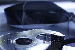 im Vordergrund Klebeband-Abroller mit Silberband, im Hintergrund durchsichtige und fast opake schwarze Mikrofilmreste