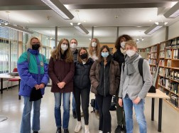 8 Jugendliche mit Maske im Lesesaal des Archivs blicken in die Kamera.