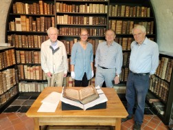 Vier Personen stehen vor einem aufgeklappten alten Buch