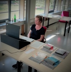 Foto: Frau Jäger sitzt vor einem Laptop, neben ihr liegen Bücher auf dem Tisch