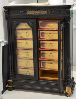 Foto: Ein alter halbhoher Schrank aus dunklem Holz mit zwei Glastüren und Fächern