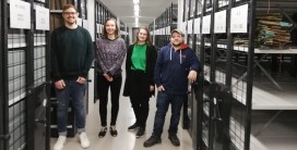 Vier Personen stehen im Gang zwischen Regalen mit Archivgut