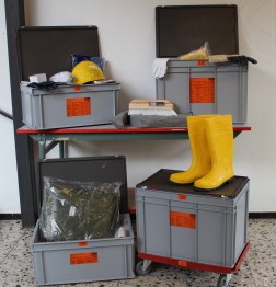 4 graue Boxen mit Inhalt: gelber Helm, Gummistiefel, Bürsten und anderes